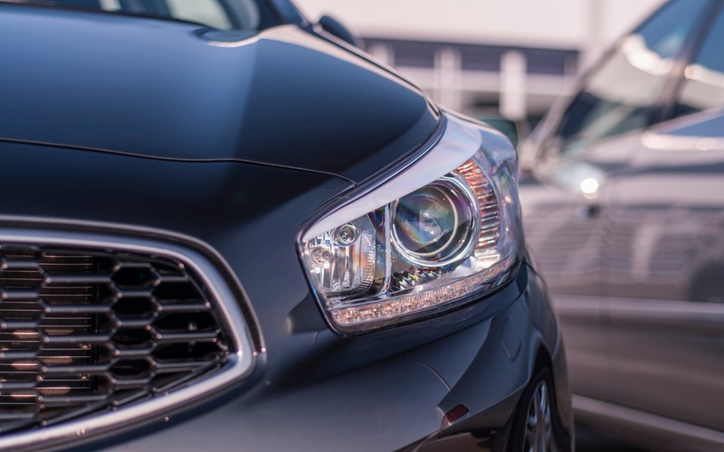 A close-up of the front grille and headlight of a dark blue Subaru car with a silver car blurred behind it.