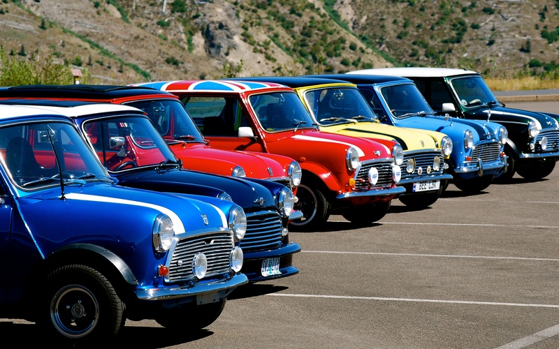 A lineup of classic Mini Cooper cars of various colors, including blue, red, and yellow, parked next to one another.