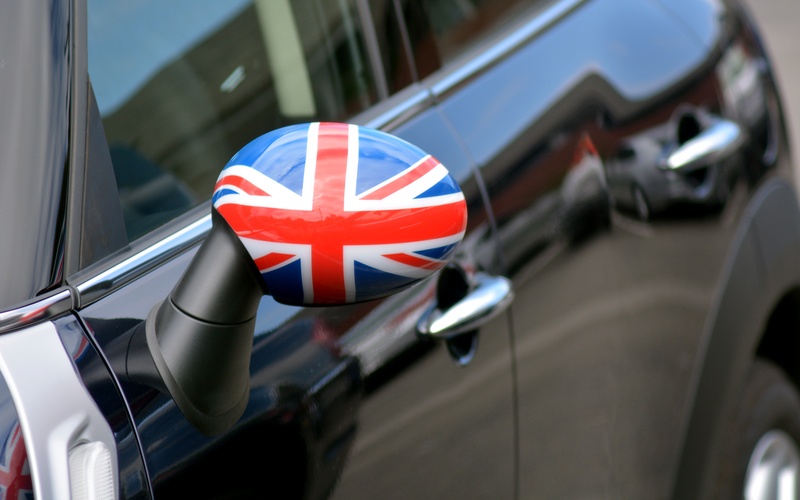 A close-up of the side mirror of a blue modern Mini Cooper with the Union Jack British flag on the mirror.