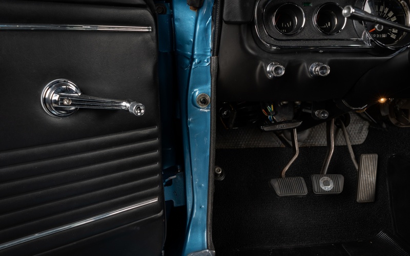 The driver's seat of a classic car with the door open showcases the driver's clutch, brake, and gas pedals.