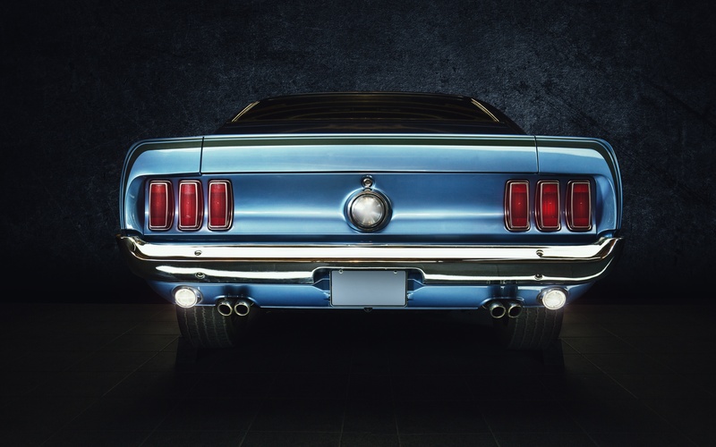 The rear end of a powder blue classic Ford Mustang, featuring taillights, exhaust pipes, and the gas cap.