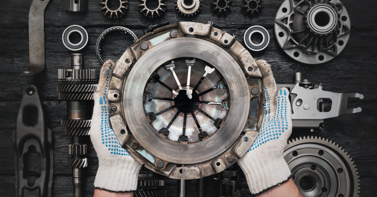 An overhead view of a person's hands with gloves holding up an old clutch basket over a table of various clutch components.