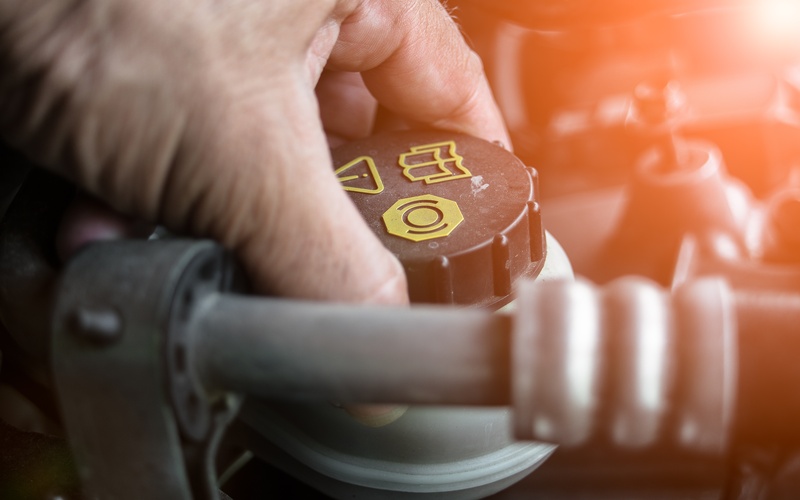 A close-up of a man's hand clasping the blake and yellow cap of a car's reservoir for brake and clutch fluid.