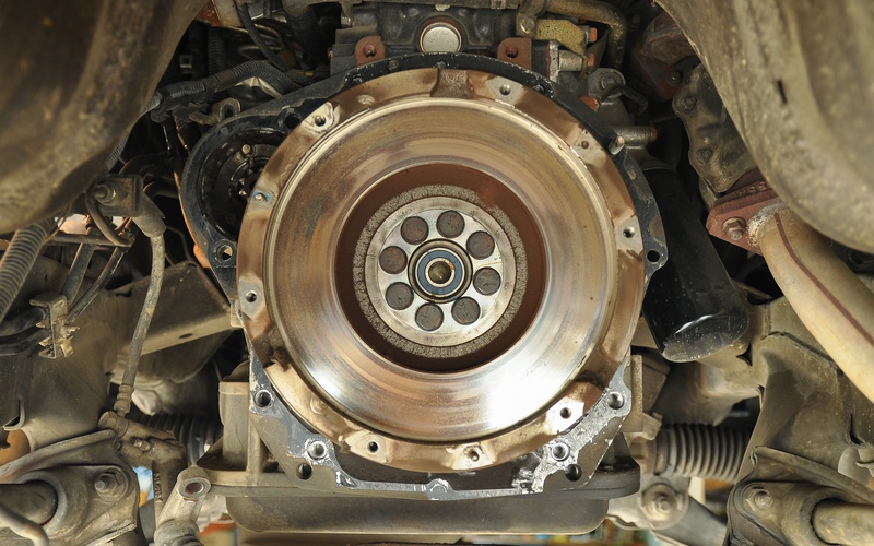 A close-up of the undercarriage of an old mini truck engine with the clutch exposes to show the flywheel.