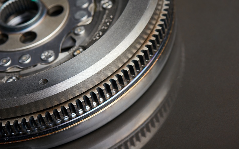 A close-up of a section of a dual-mass flywheel for a clutch vehicle, showcasing its grooved teeth on a black surface.