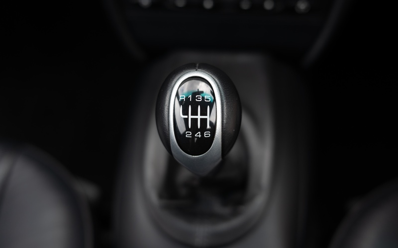 A close-up of a modern manual transmission car's gear stick selector. The stick has six speed gears and a reverse gear.