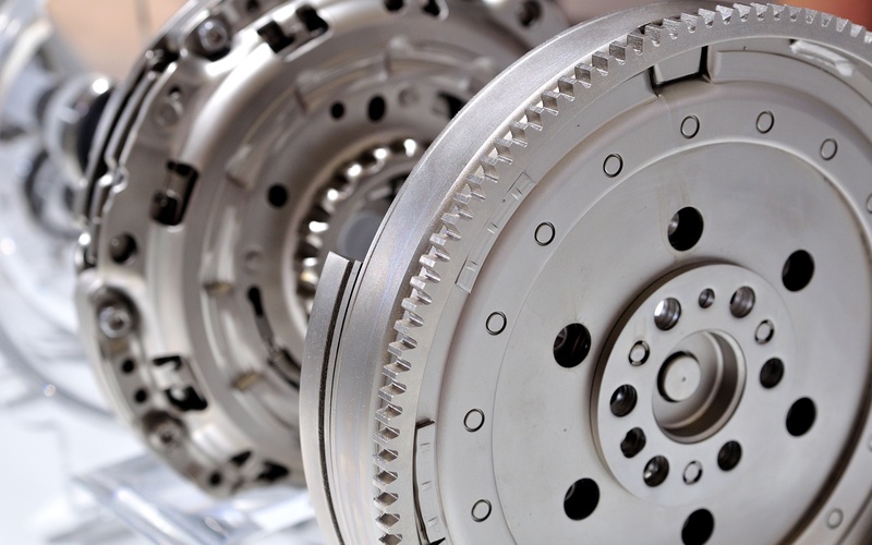 A close-up of a new automotive flywheel for a manual clutch transmission on display in a plastic case.
