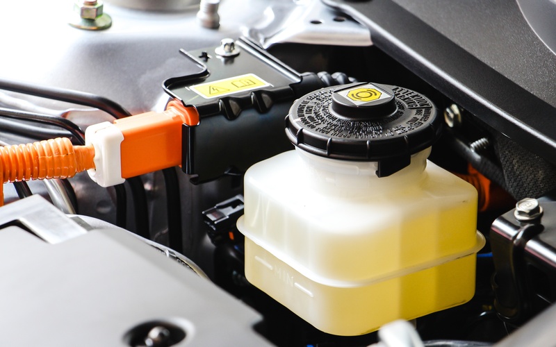 A close-up of the brake and clutch fluid reservoir in the engine compartment of a car with a yellow, transparent fluid.