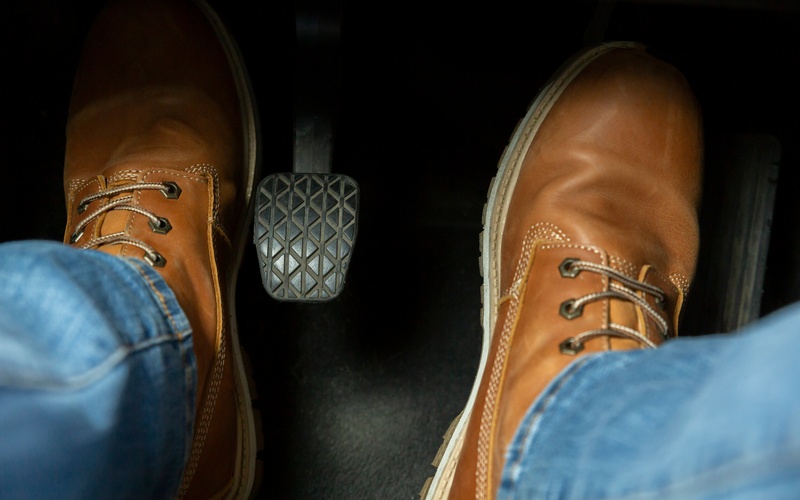 A close-up of a person's feet in the driver-side compartment, with one foot pressing the clutch pedal.