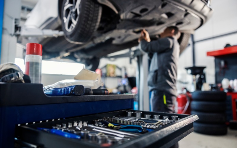 A close-up of a mechanic's toolbox while a man works on the undercarriage of a car on an elevated lift.