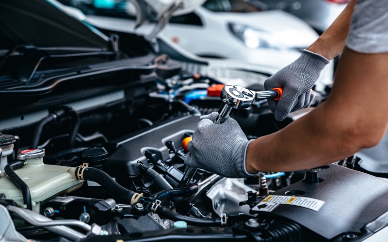 A close-up of a man's hands with gloves using a torque wrench to adjust a part inside the engine of a car.