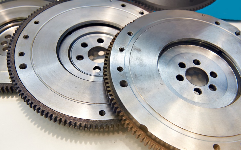 A close-up of three automotive flywheels layered on one another on a white table next to a blue wall.