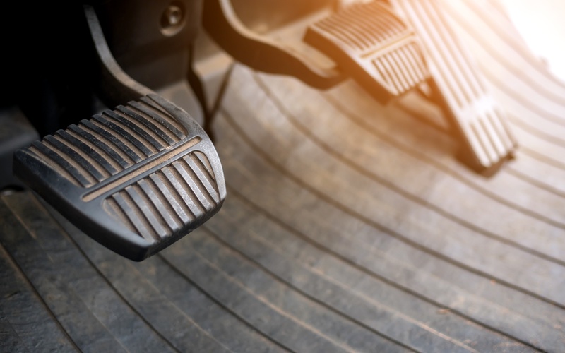 A close-up of the pedals of a manual clutch car, with a focus on the clutch pedal with the gas and brake behind it.