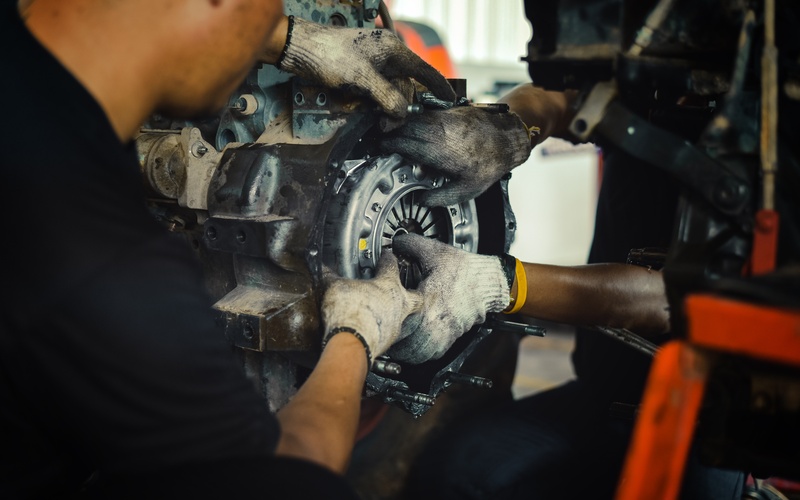A close-up of two mechanics with gloves holding the clutch disc in place in an engine removed from the car.