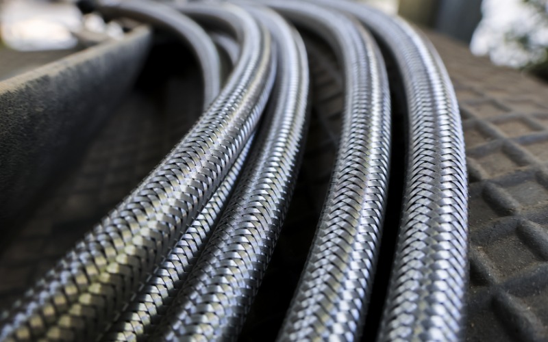 A close-up of six stainless steel braided hydraulic hose lines together on a hard black plastic surface.