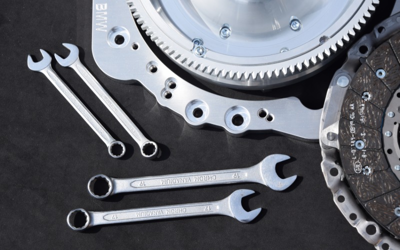 A close-up of the clutch disc and flywheel cover of a new clutch kit on a black table with four wrenches.