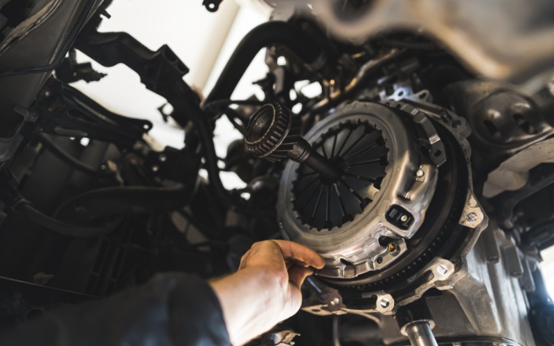 A view from below looking up at the undercarriage of a car's transmission, with a hand reaching to adjust the clutch.