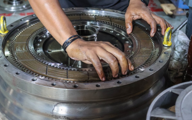 A close-up of a pair of hands installing a clutch disc into a disconnected automatic car transmission.