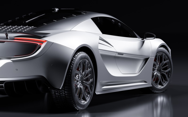 A rear view of a silver two-door coupe sports car on a grey, reflective surface with a black background.
