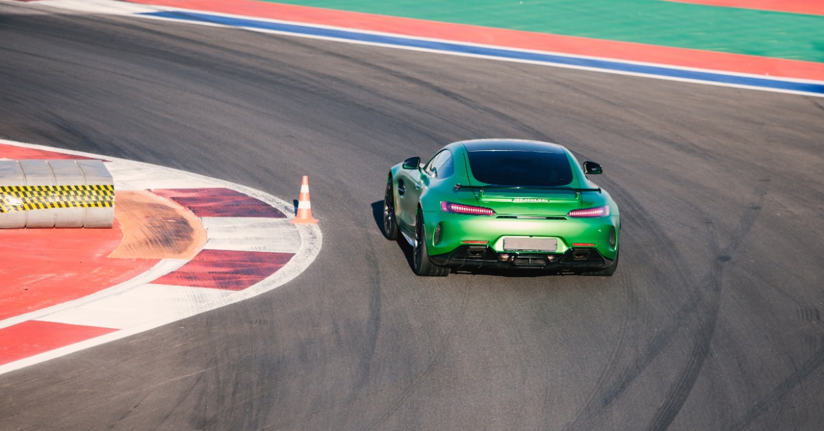 A rear view of a green, two-door sports car coupe with a spoiler hitting the apex of a corner of a racetrack.