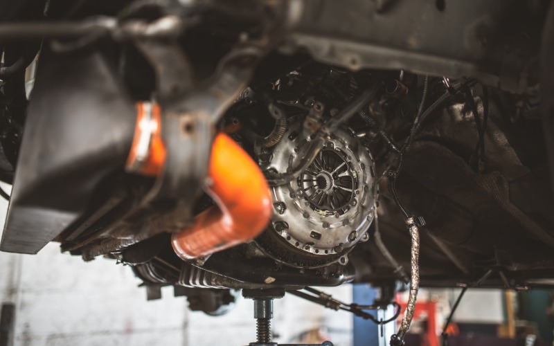 A close-up view from below of the transmission and clutch assembly of a car while elevated on a lift in a repair shop.
