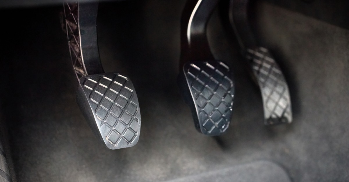 A close-up of the gas, brake, and clutch pedals at a driver's feet in a manual transmission vehicle.