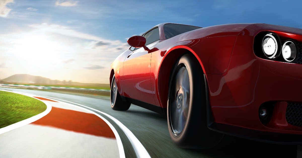 A low-angle view of a two-door, red sports car navigating the corner of a racetrack with racing curbs on a sunny day.