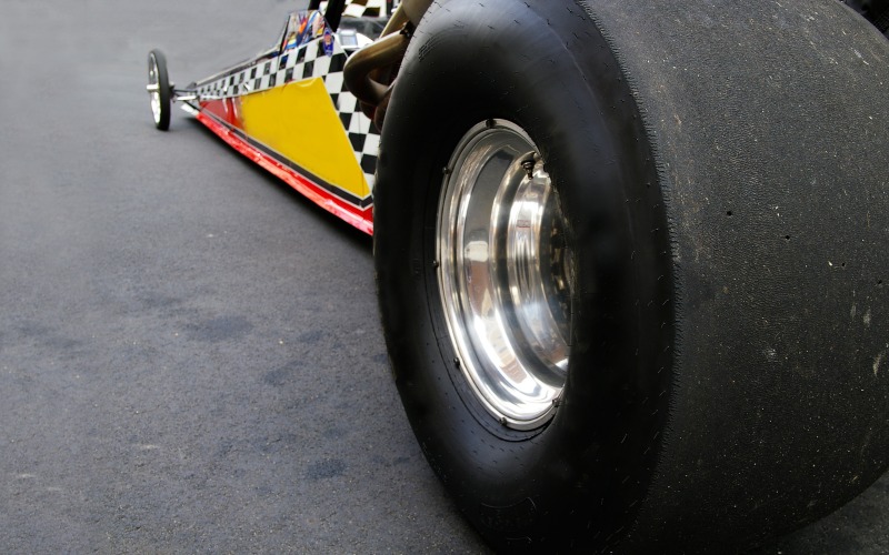 A close-up of the rear-wheel tire and side chassis of a drag racing racecar with a checkered flag pattern.