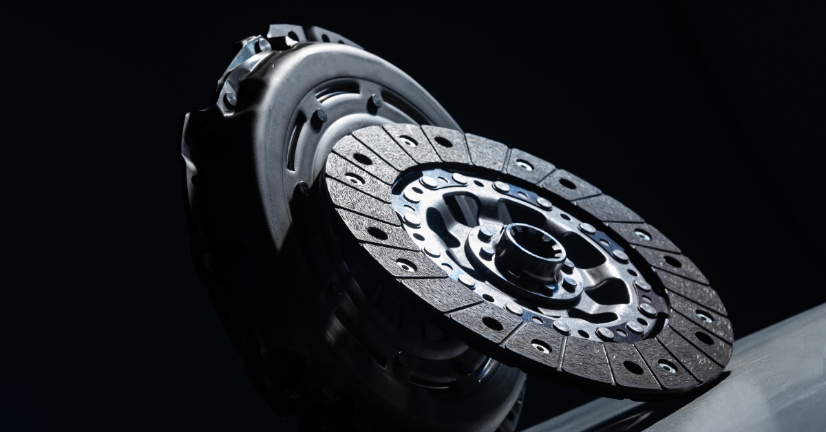 A close-up of a new black clutch disc propped up and leaning against a clutch basket against a black background.