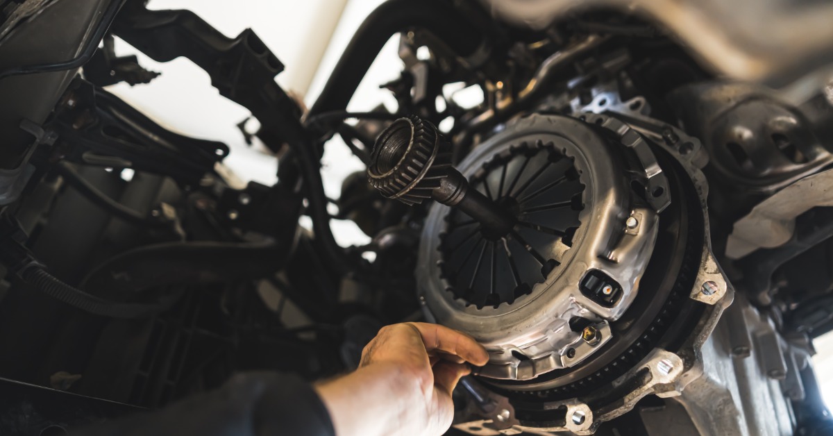 A close-up of the undercarriage of a vehilce elevated on a lift as a man's hand reaches to install a new clutch kit.