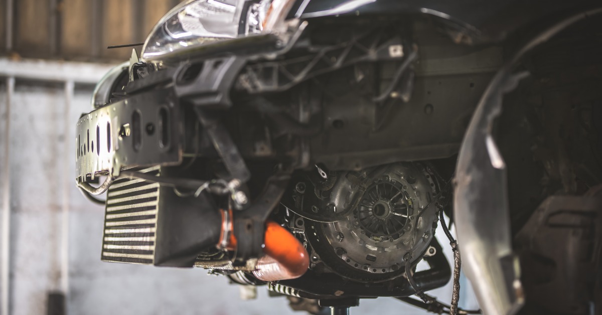A close-up of the side of a car elevated on a lift and disassembled to show the intercooler and clutch.