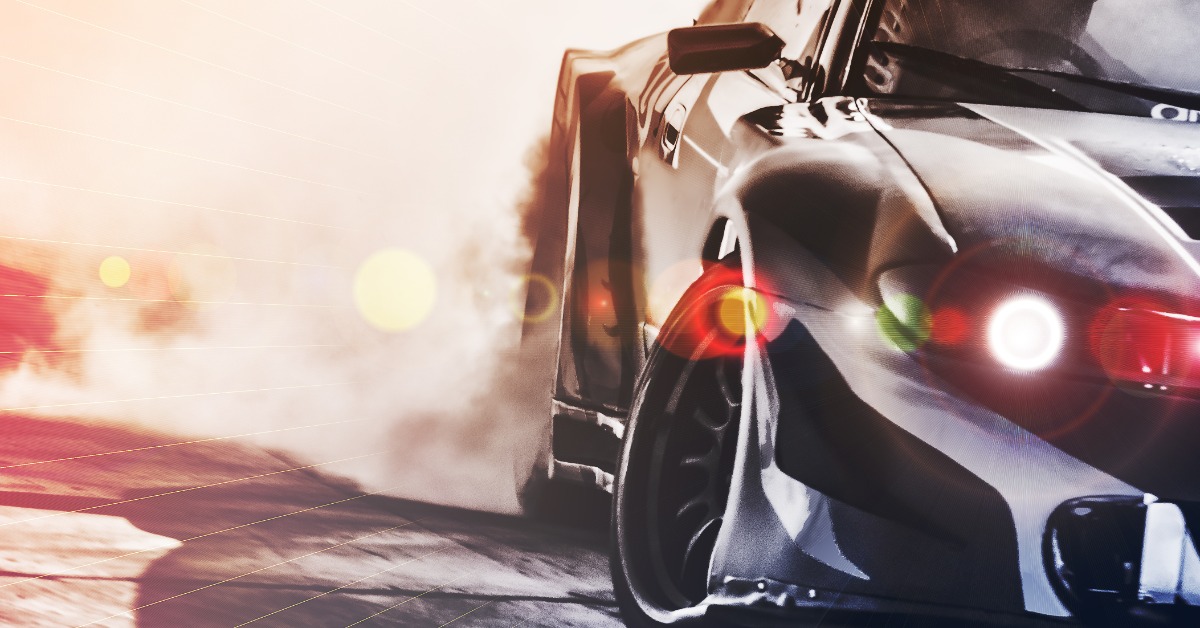 A close-up of a black sports car with activated headlights drifting around a corner and producing smoke from the tires.