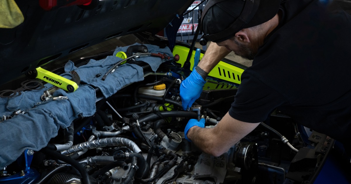 A man with latex gloves working on the engine of a high-performance car with the neon hood up and various tools around.