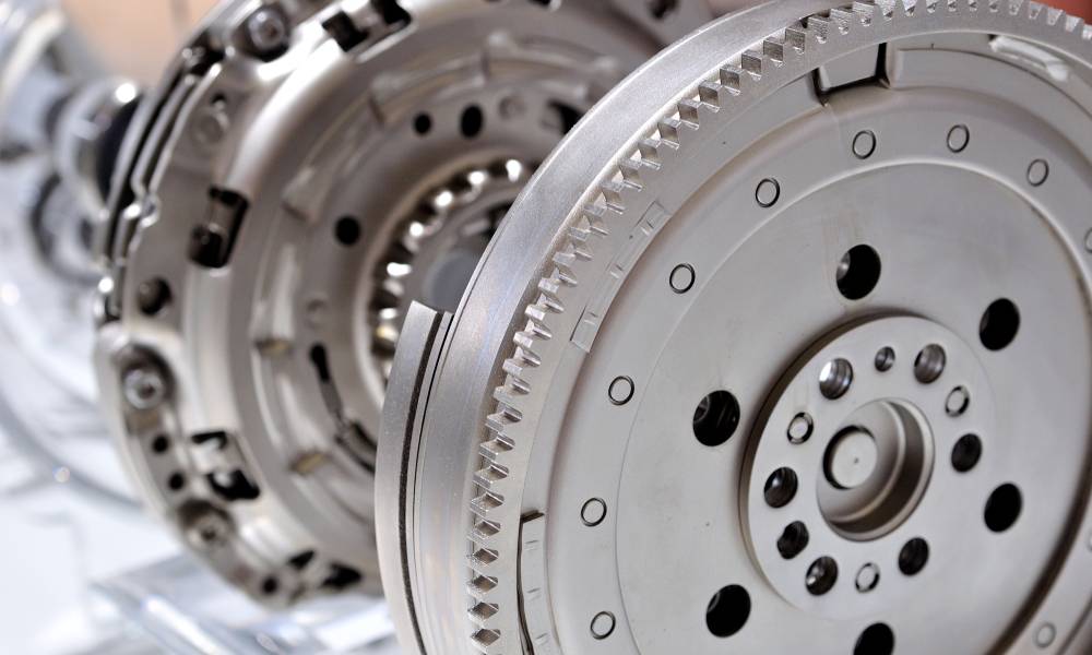 A steel automotive flywheel displayed vertically disconnected from the engine next to an automotive clutch.