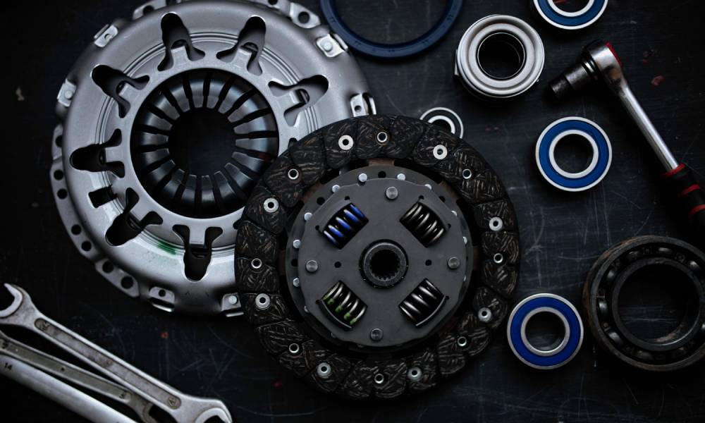 A new clutch kit on a black table with the flywheel resting on top of the kit with wrenches and other tools around it.