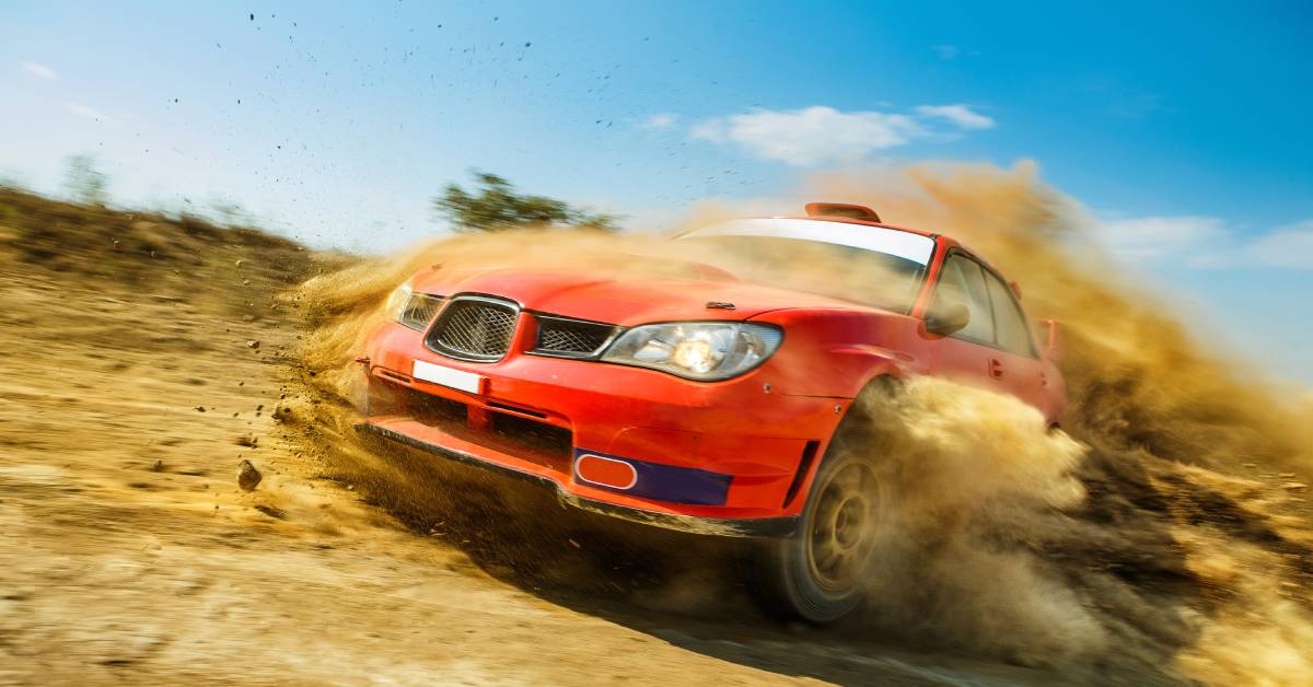 A red, Subaru rally car with a racing spoiler drifting around a dirt rally track and kicking up dirt and debris.