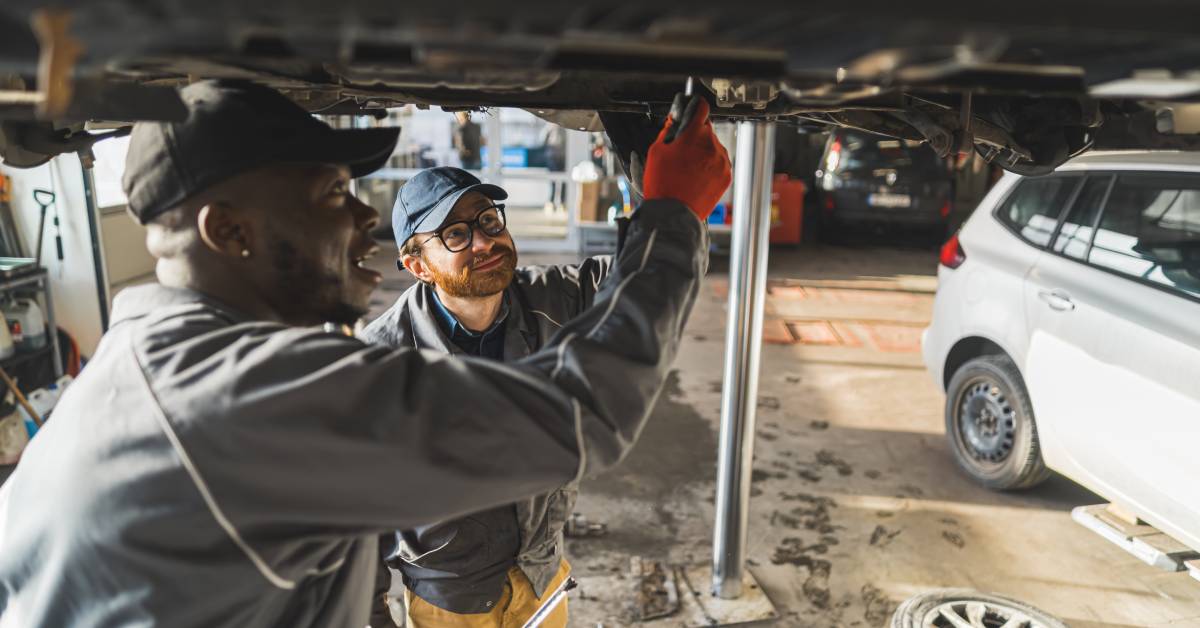 Two male mechanics are inspecting and working on a vehicle on a lift together with tools in an auto service shop.