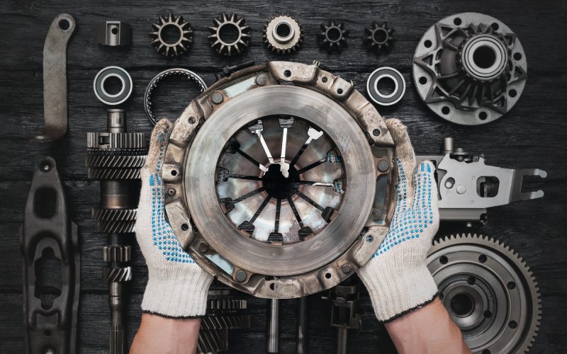 An overhead veiw of a mechanic with gloves holding a clutch basket over a table featuring other parts of an auto clutch.