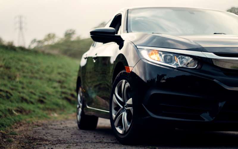 The right half of a black Honda Civic sedan with its headlights on, windows down, and a green hill behind it.