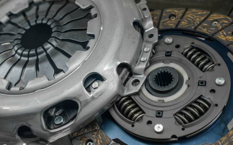 A light grey clutch cover is overlapping and stacked on top of a stock automotive clutch basket.