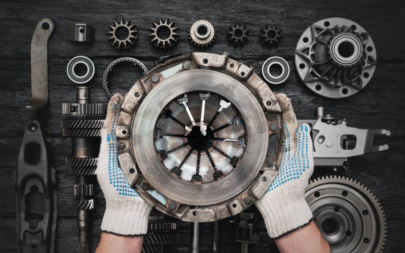 An overhead view of a mechanic holding a used vehicle clutch basket over a table with various clutch parts.