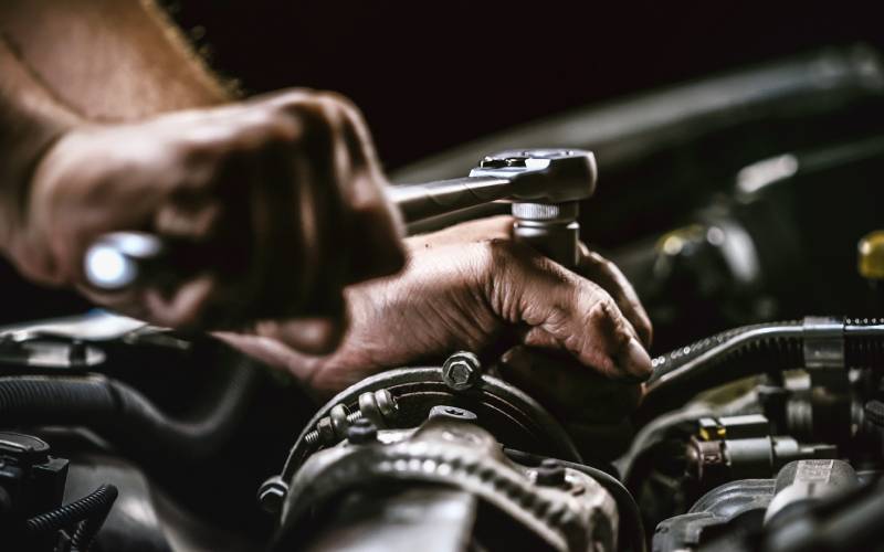 A close-up of a mechanic's hands twisting a socket wrench to tighten a nut on an automotive engine.