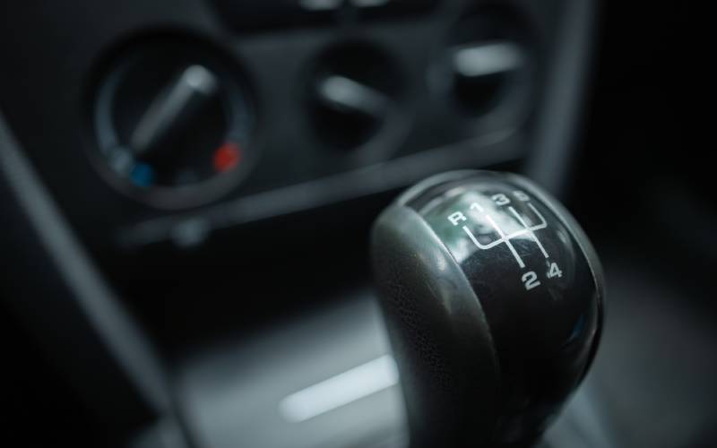 A close-up of a car's manual gear stick of a manual transmission vehicle showing gears one through four and reverse.