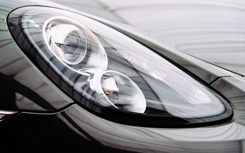 A close-up view of the curved glass and socket of a black Porsche car headlight featuring the sidelight.