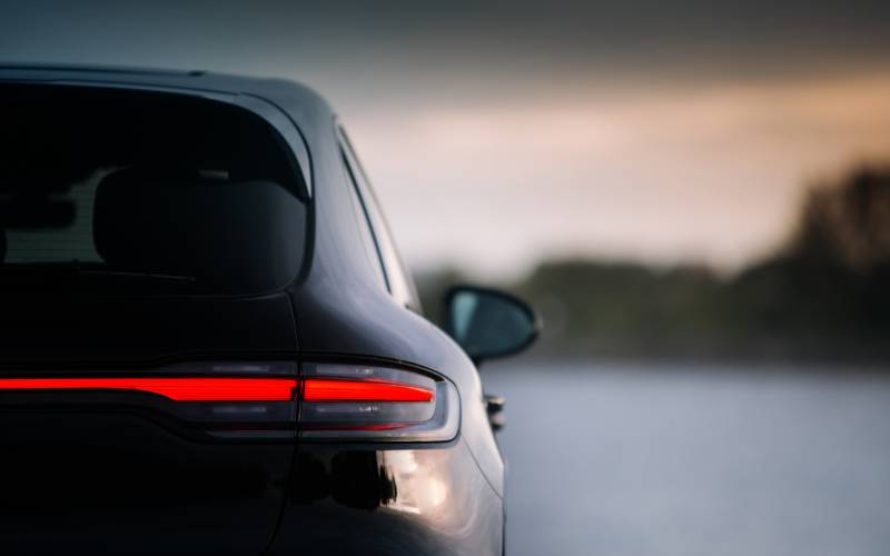 A rear quarter view of a black Porsche car with tail lights activated in focus with the background blurred.