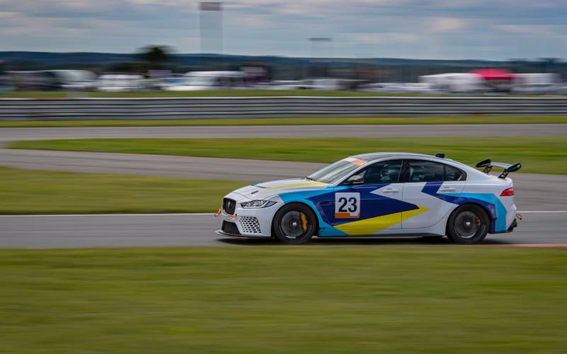 A sie view of a white, blue, and yellow race car with a spoiler and the number 23 racing around a circuit track.