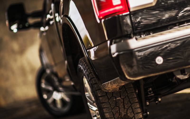 A close-up of the rear bumper and tire of a black heavy-duty, modern pickup truck with aluminum-alloy rims.