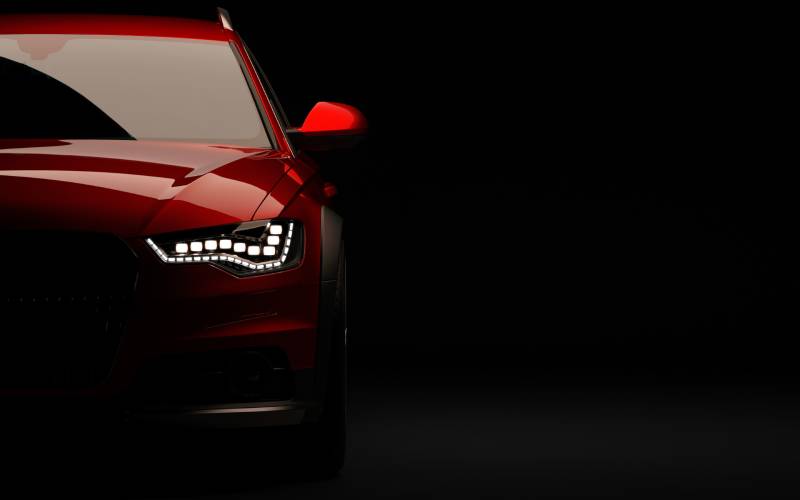 A front half view of a red Audi car with the distinctive Audi headlights activated against a black background.