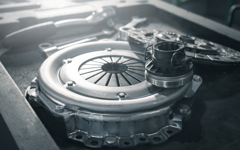 A new clutch kit for a vehicle is sitting on a workbench. A flywheel and hand tools are next to it.