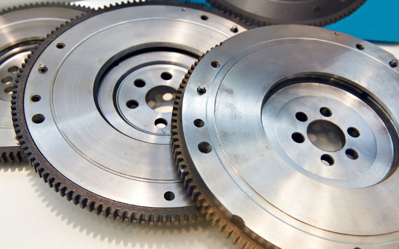 A series of three crankshaft automotive flywheels stacked and overlapping one another on a white table.